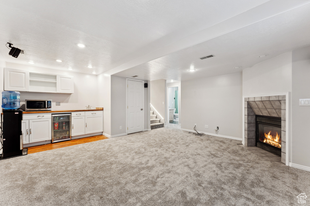 Unfurnished living room featuring beverage cooler, light carpet, bar, stairway, and recessed lighting