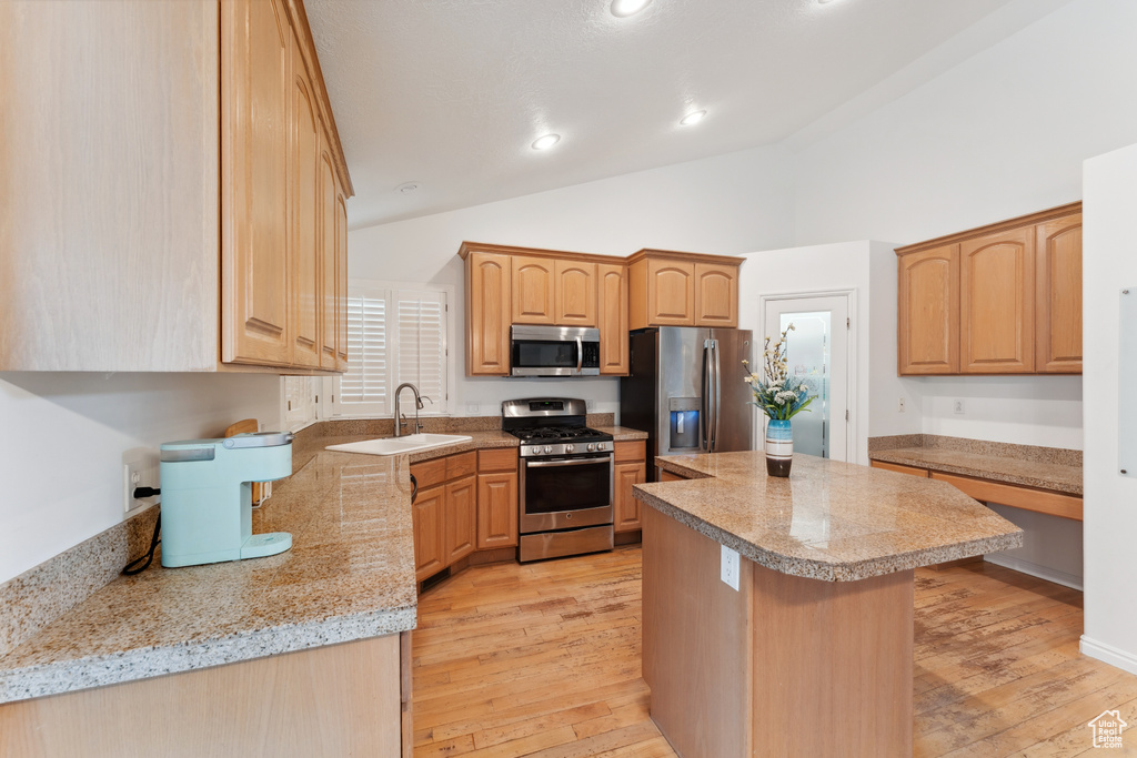 Kitchen featuring stainless steel appliances, a sink, light countertops, a kitchen island, and light wood finished floors