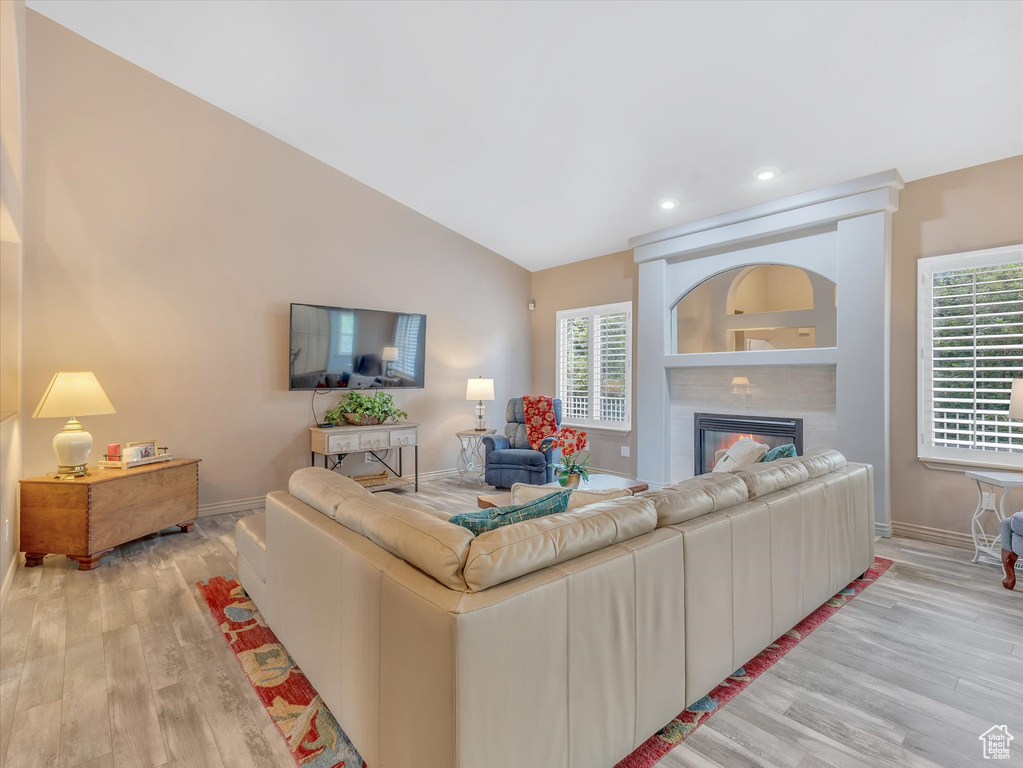 Living area featuring light wood-style floors, a glass covered fireplace, baseboards, lofted ceiling, and recessed lighting