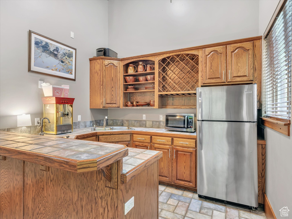 Kitchen featuring appliances with stainless steel finishes, tile countertops, a sink, open shelves, and a peninsula