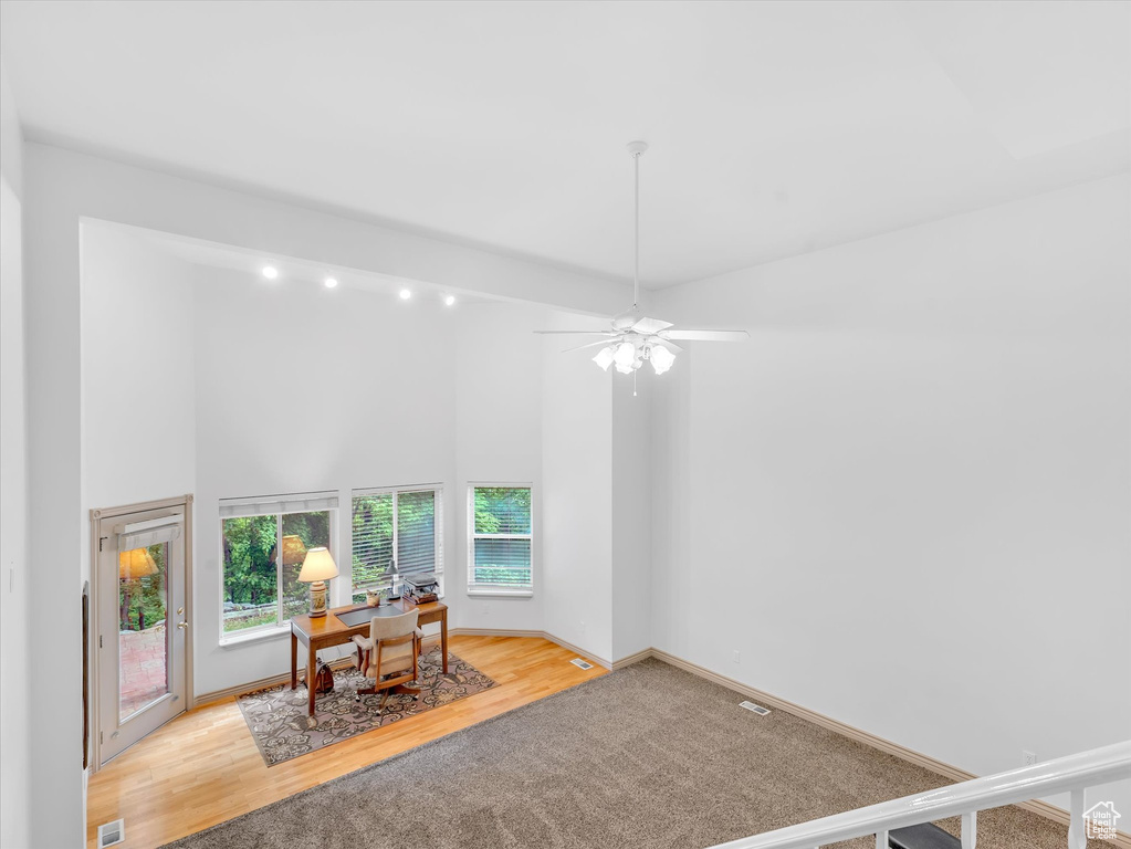 Office area featuring a high ceiling, wood finished floors, ceiling fan, baseboards, and carpet