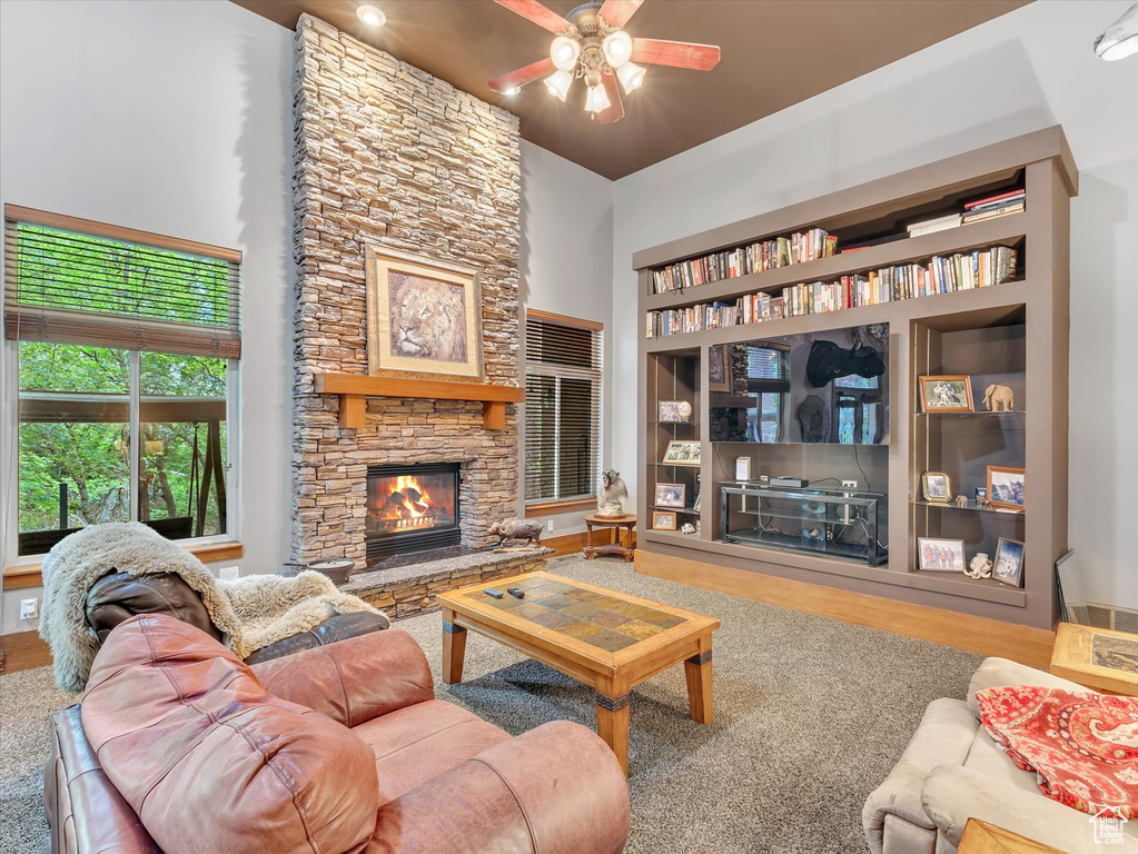 Living area featuring a stone fireplace, a ceiling fan, a high ceiling, wood finished floors, and built in shelves
