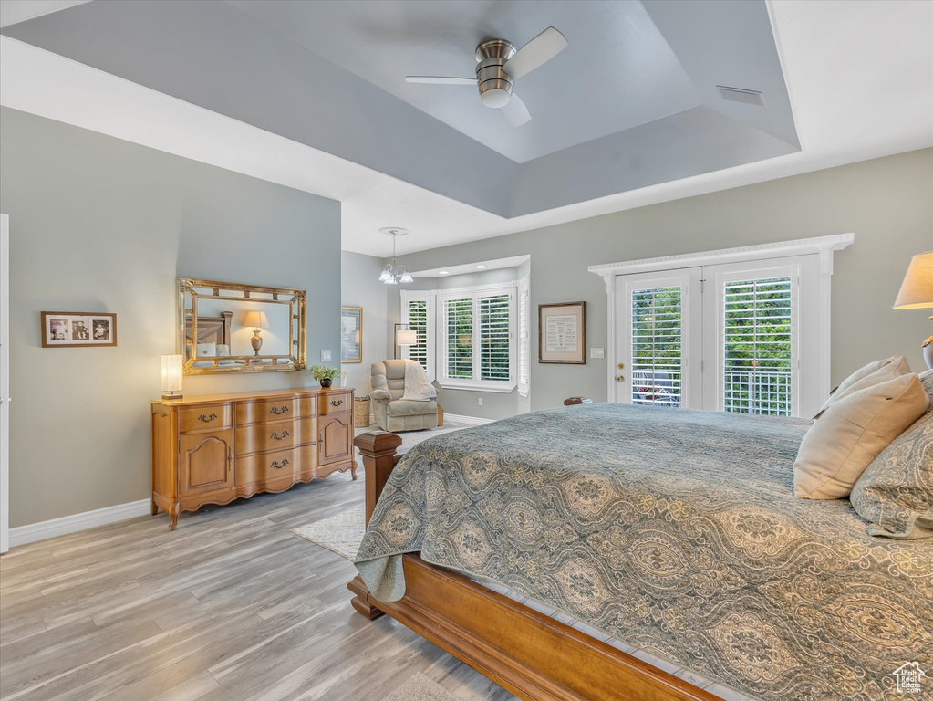 Bedroom featuring access to outside, light wood finished floors, baseboards, a tray ceiling, and a ceiling fan