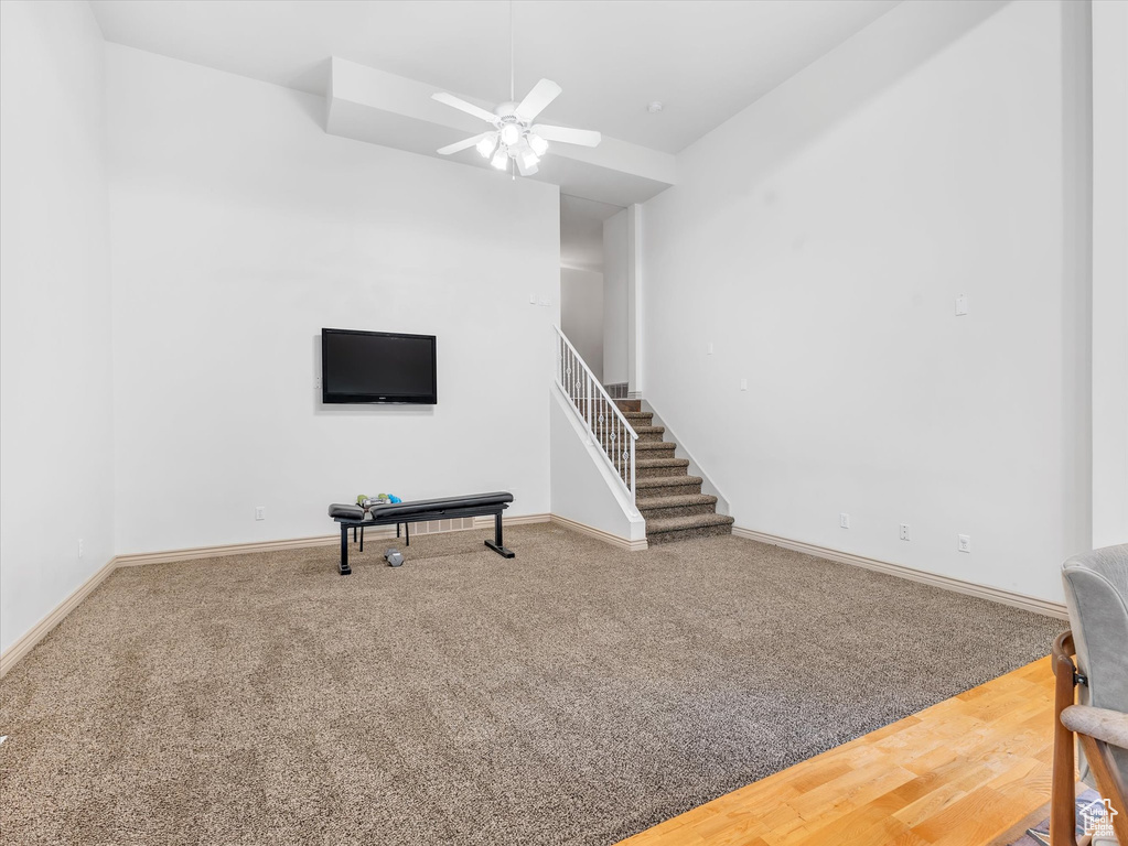 Unfurnished living room with carpet floors, baseboards, ceiling fan, and stairs