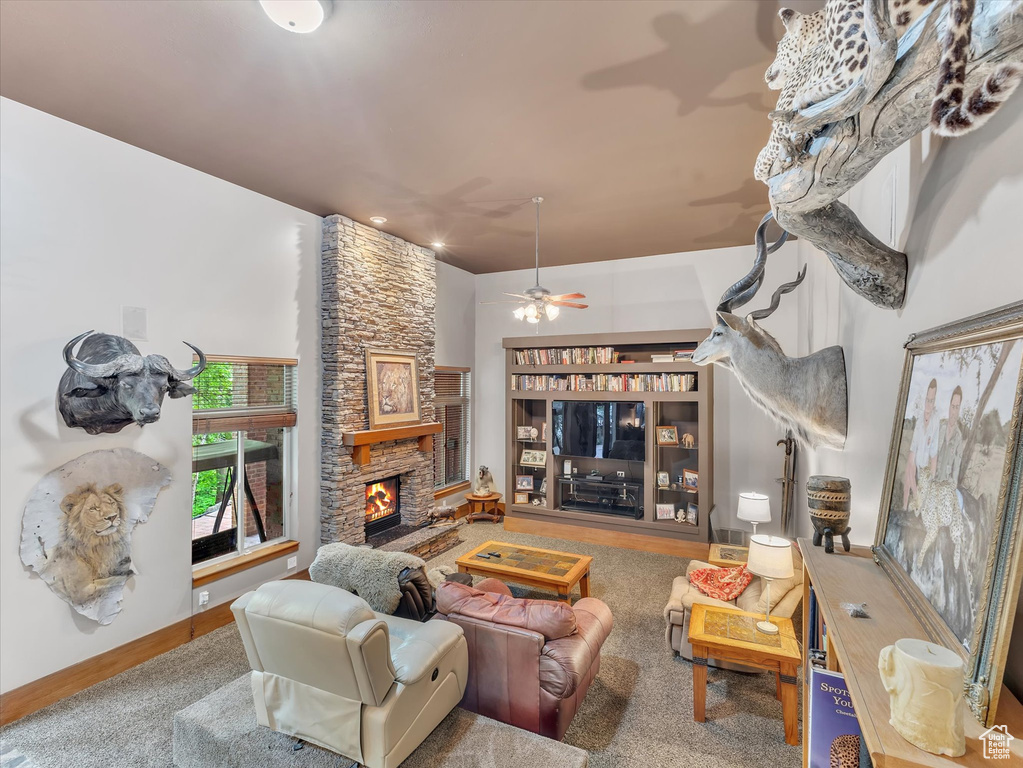 Living room featuring a stone fireplace, ceiling fan, and baseboards