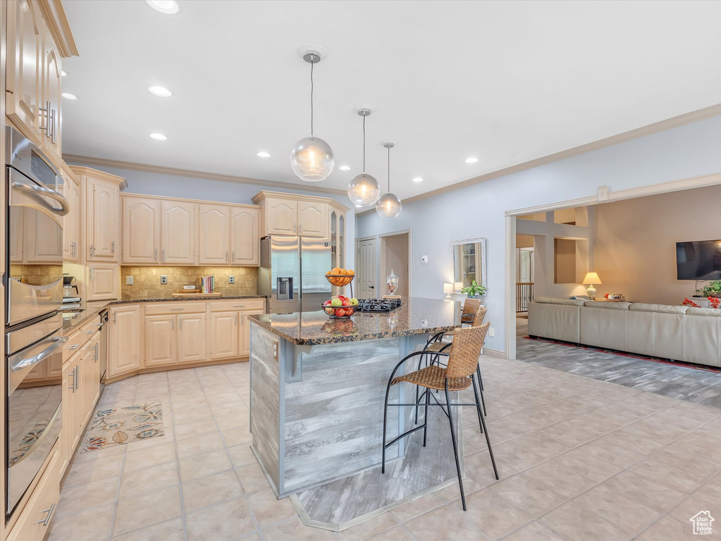 Kitchen with appliances with stainless steel finishes, a breakfast bar area, crown molding, dark stone counters, and backsplash