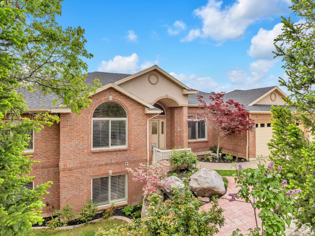 View of front facade featuring a garage, a shingled roof, brick siding, and stucco siding