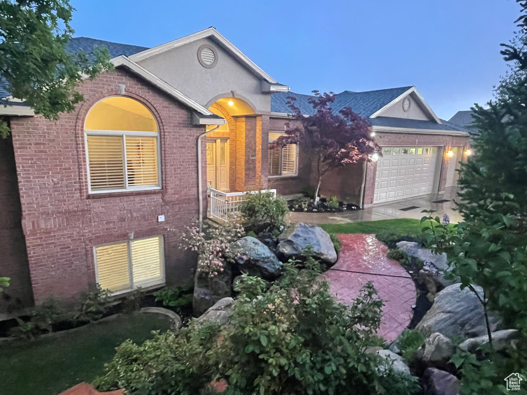 View of front of house featuring brick siding, an attached garage, and stucco siding