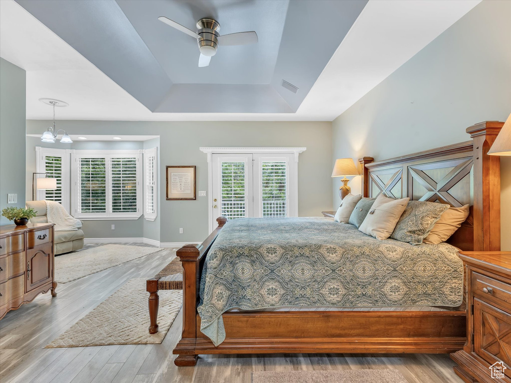 Bedroom featuring a tray ceiling, wood finished floors, access to outside, baseboards, and a chandelier