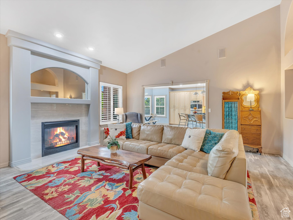 Living area featuring light wood-type flooring, baseboards, a tiled fireplace, high vaulted ceiling, and recessed lighting