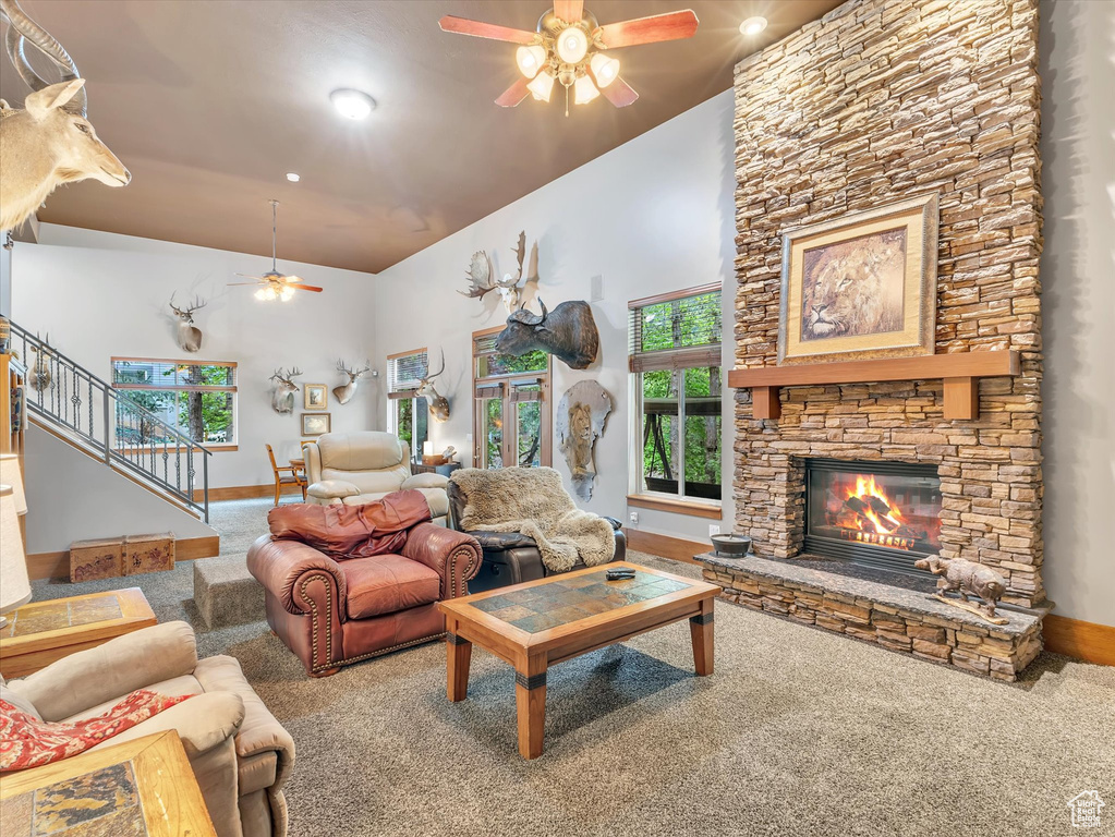 Living room featuring ceiling fan, carpet, a stone fireplace, baseboards, and stairway