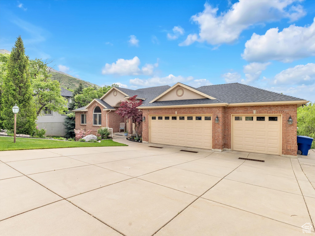 View of front of home with driveway, a garage, brick siding, roof with shingles, and a front lawn