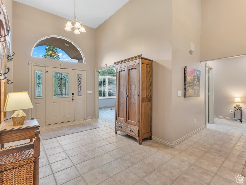 Foyer featuring a towering ceiling, a chandelier, light tile patterned floors, and baseboards