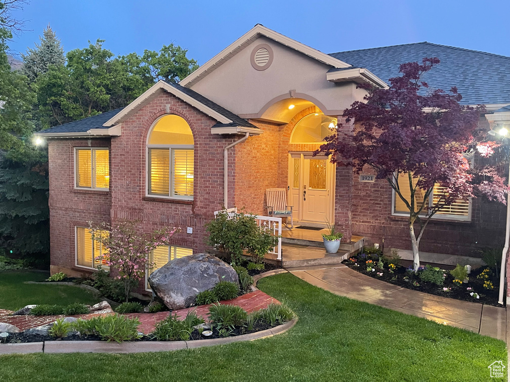 View of front of home with brick siding, a front yard, and a shingled roof