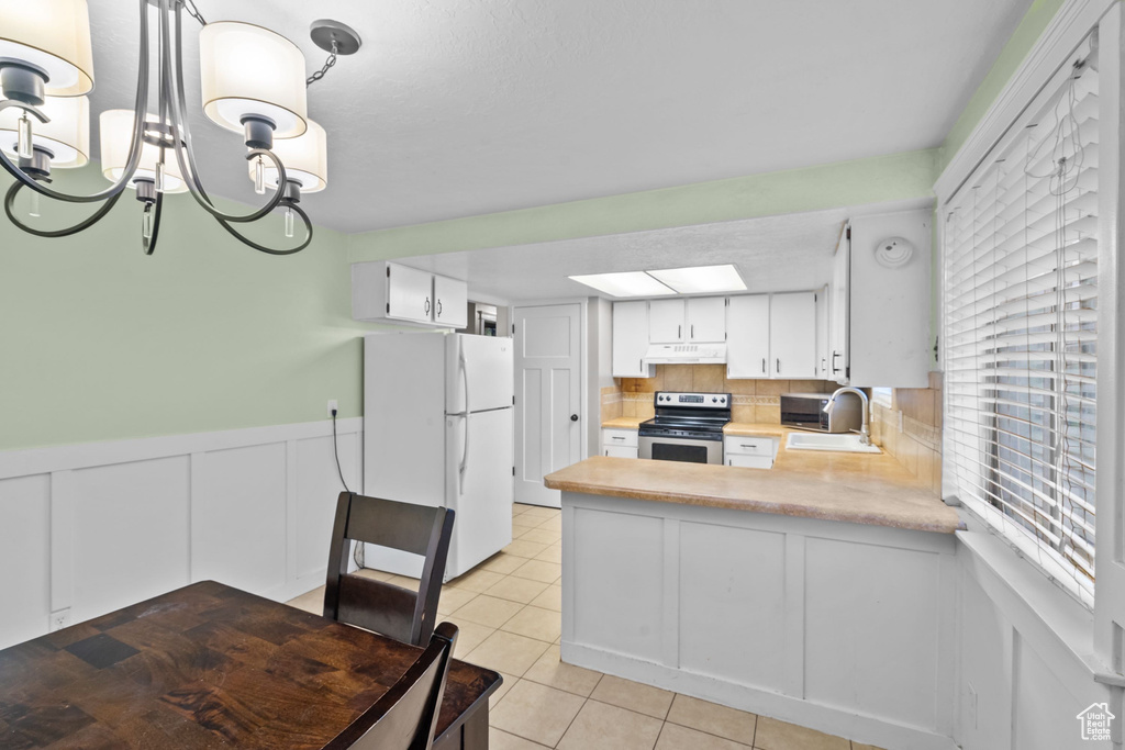 Kitchen featuring freestanding refrigerator, stainless steel electric stove, under cabinet range hood, light countertops, and a sink