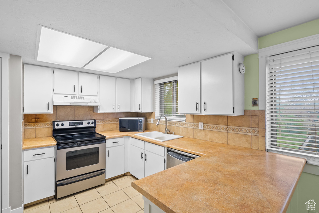 Kitchen featuring stainless steel appliances, a sink, under cabinet range hood, a peninsula, and white cabinets