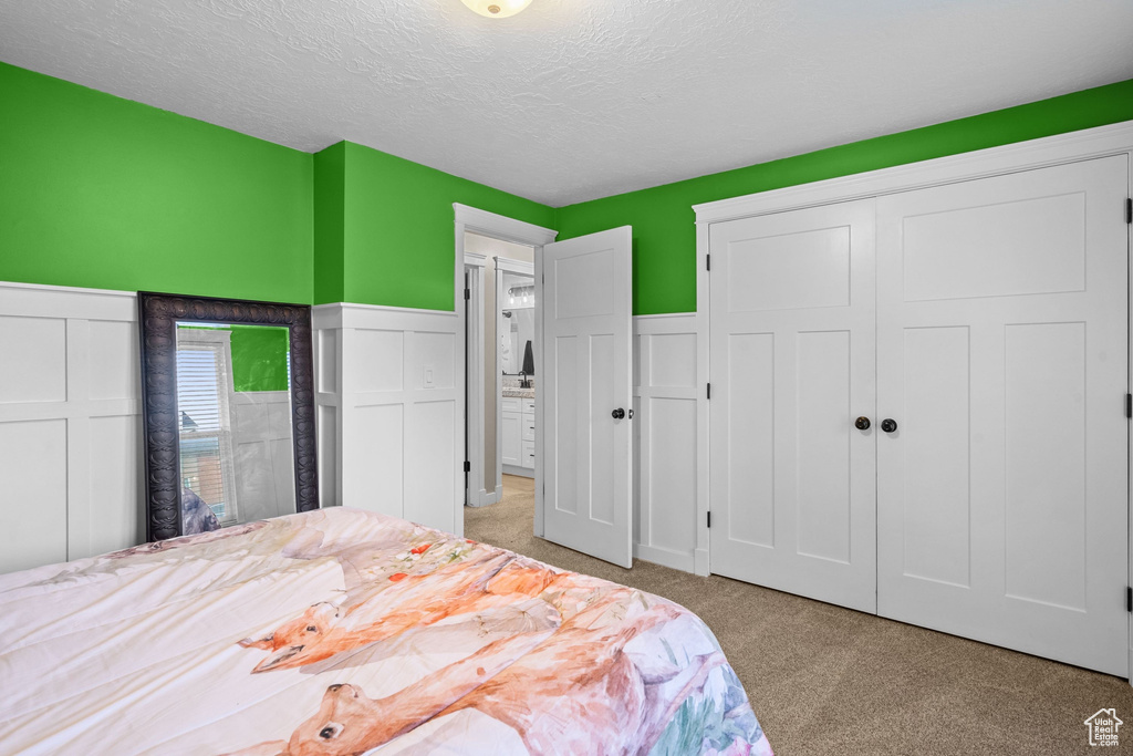Bedroom with light colored carpet, a textured ceiling, and a closet