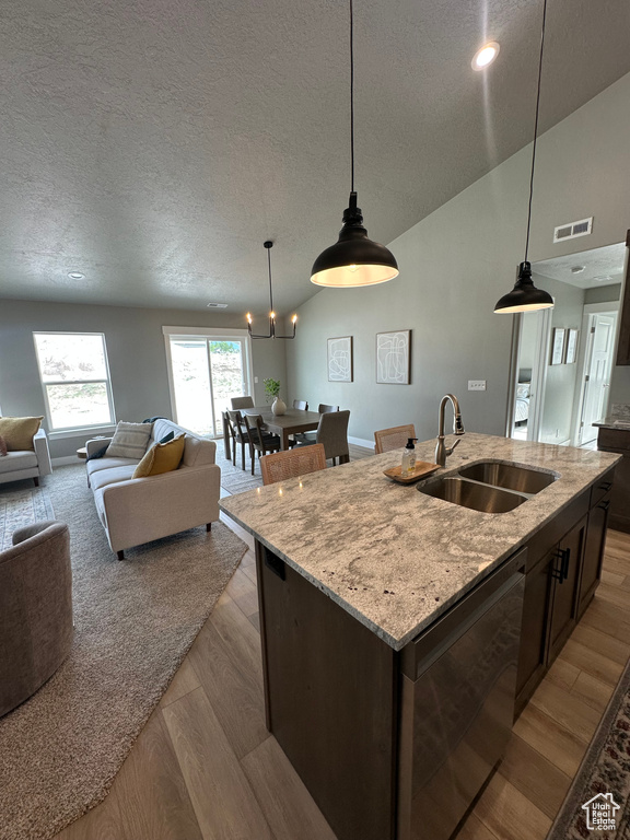 Kitchen with a sink, open floor plan, a textured ceiling, wood finished floors, and an island with sink
