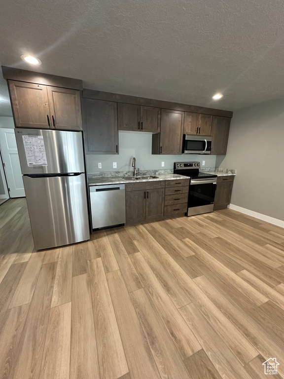 Kitchen featuring stainless steel appliances, a sink, a textured ceiling, light wood-style flooring, and baseboards