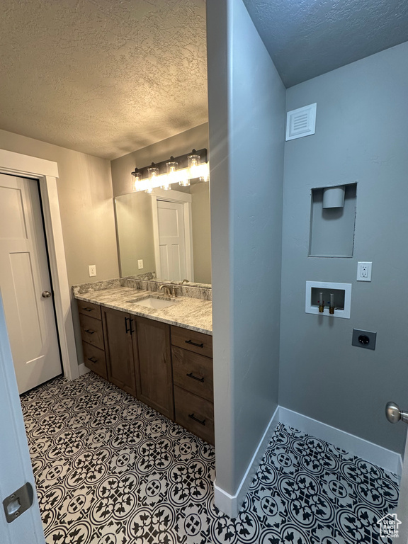 Bathroom with a textured ceiling, baseboards, and vanity