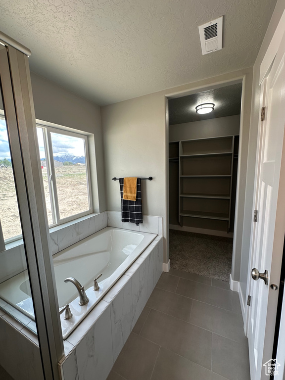 Bathroom with a textured ceiling, a spacious closet, a garden tub, tile patterned flooring, and baseboards