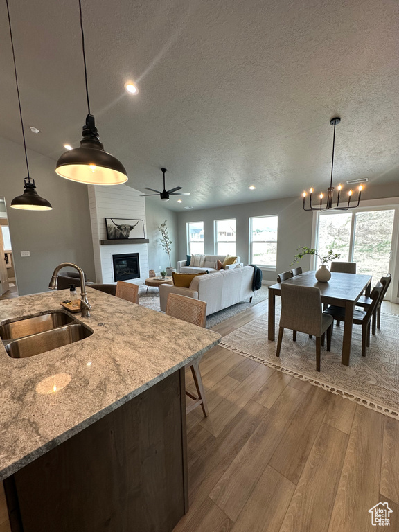 Kitchen featuring a sink, a textured ceiling, a chandelier, a large fireplace, and wood finished floors