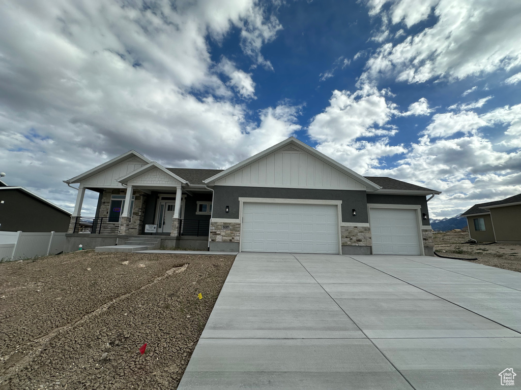 Craftsman-style house featuring a garage, covered porch, stone siding, concrete driveway, and fence