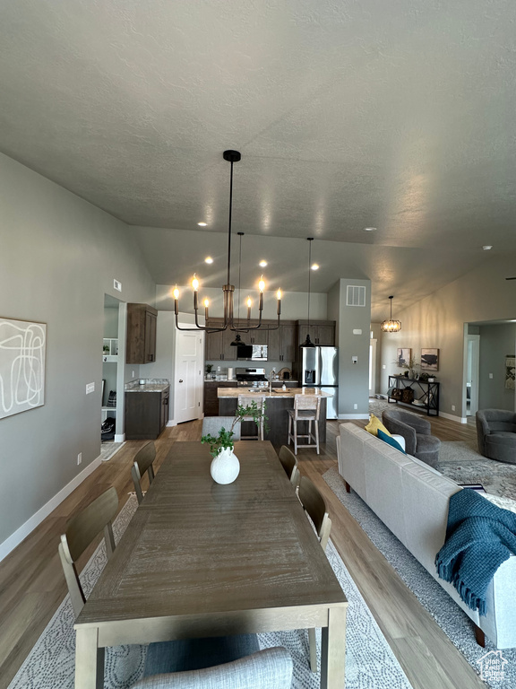 Dining room featuring vaulted ceiling, dark wood finished floors, a chandelier, baseboards, and a textured ceiling