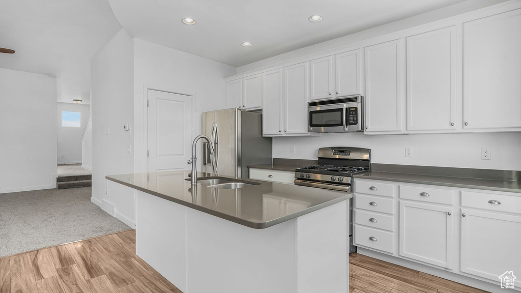 Kitchen featuring appliances with stainless steel finishes, dark countertops, an island with sink, white cabinets, and recessed lighting
