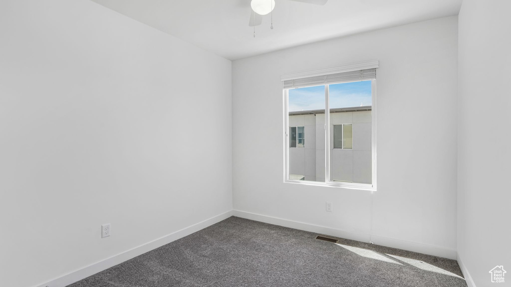 Spare room featuring ceiling fan, baseboards, and dark colored carpet