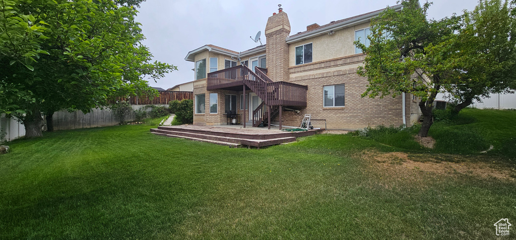 Rear view of property featuring brick siding, a deck, stairs, a chimney, and stucco siding