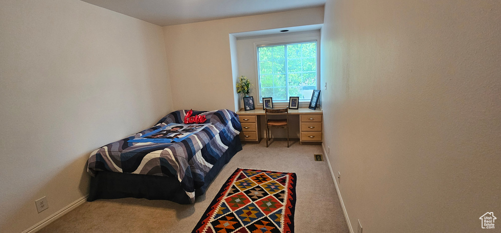 Bedroom with light colored carpet, a desk, and baseboards