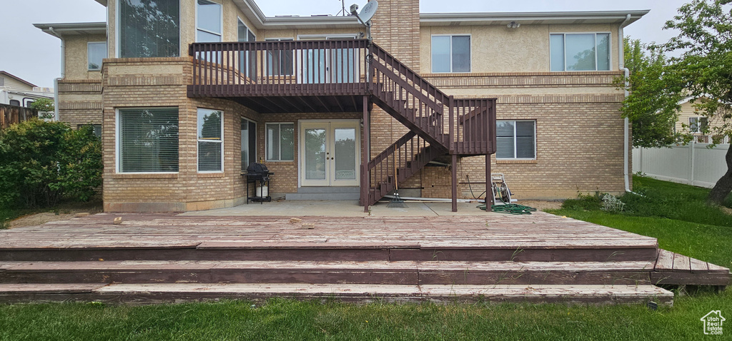 Back of property with french doors, a deck, brick siding, fence, and stairs