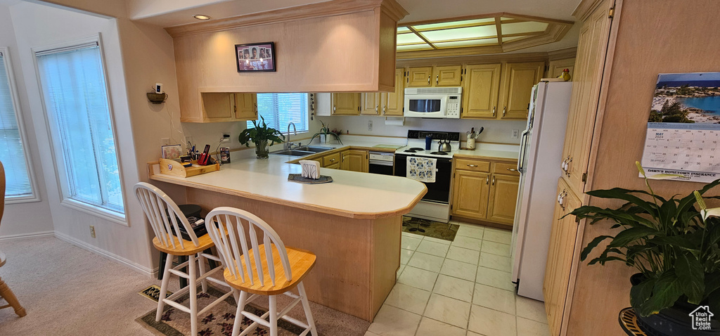 Kitchen with white appliances, a peninsula, a sink, light countertops, and a kitchen breakfast bar