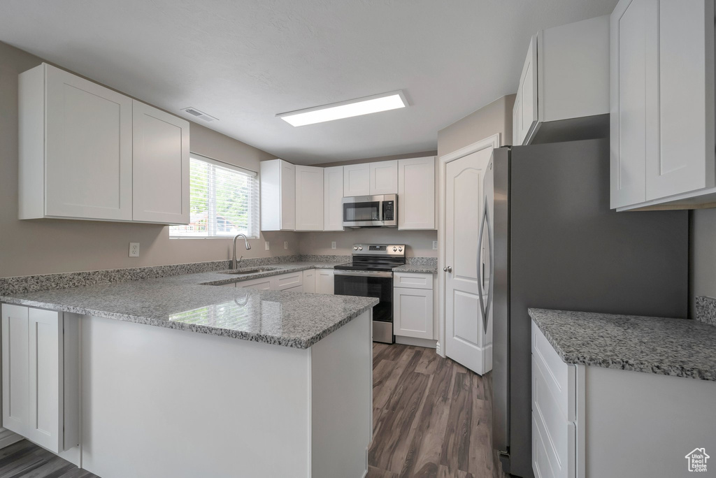 Kitchen with stainless steel appliances, a sink, a peninsula, dark wood finished floors, and white cabinets