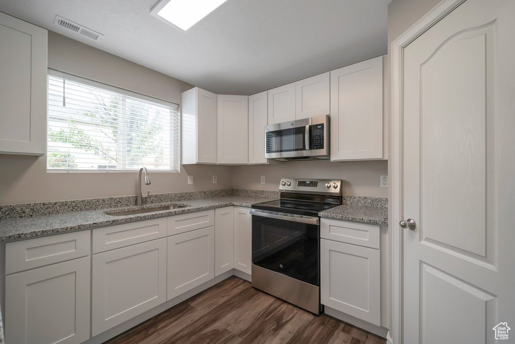 Kitchen with appliances with stainless steel finishes, a sink, dark wood-type flooring, and white cabinetry