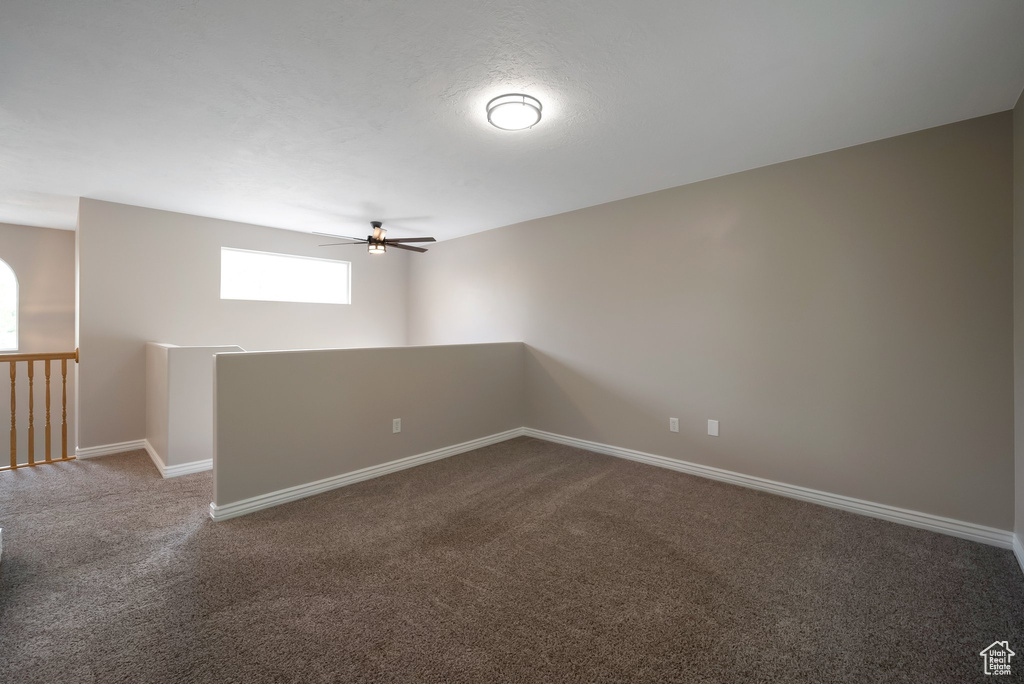 Empty room featuring dark carpet, a ceiling fan, and baseboards