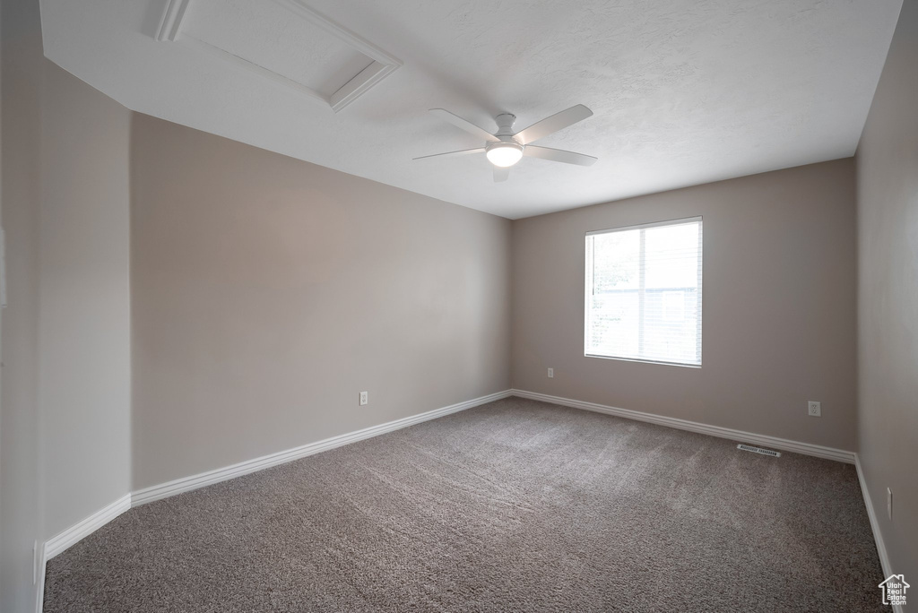Spare room featuring carpet floors, attic access, baseboards, and a ceiling fan