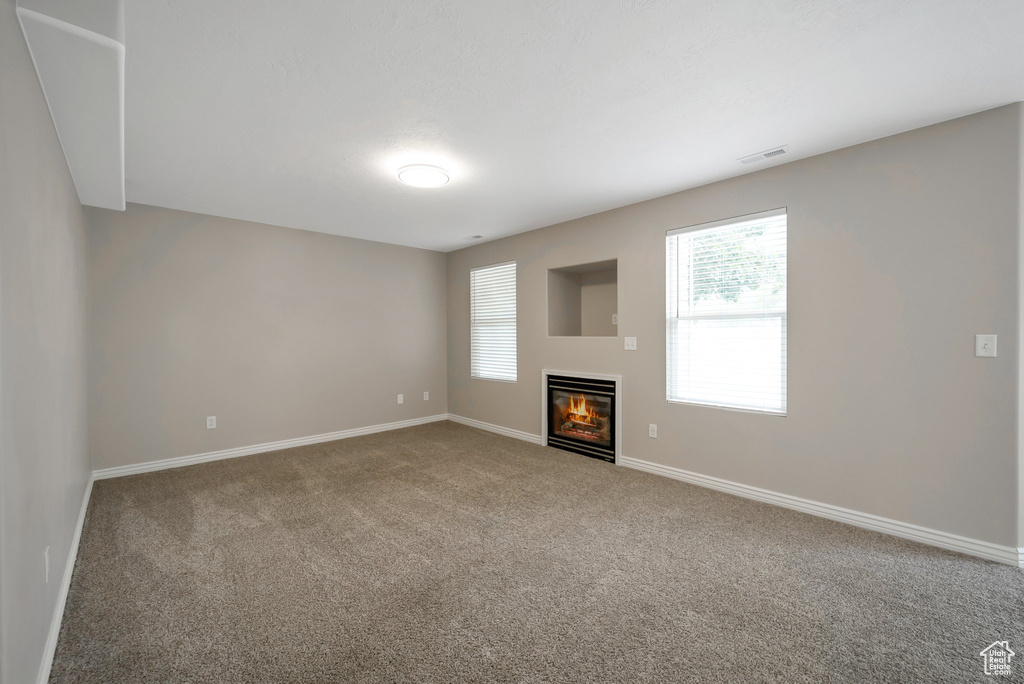 Unfurnished living room with carpet, baseboards, and a glass covered fireplace