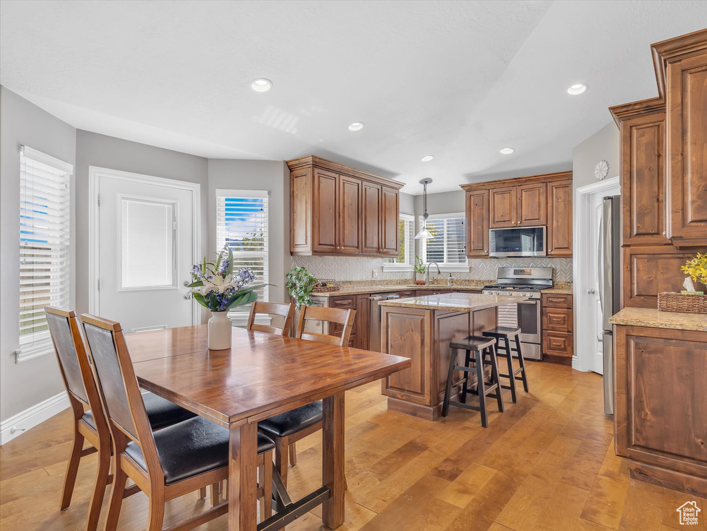 Kitchen with appliances with stainless steel finishes, a kitchen island, tasteful backsplash, a sink, and light wood finished floors