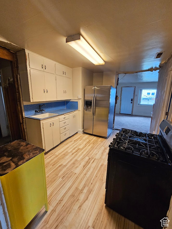 Kitchen featuring stainless steel appliances, light wood-style flooring, white cabinets, and a sink