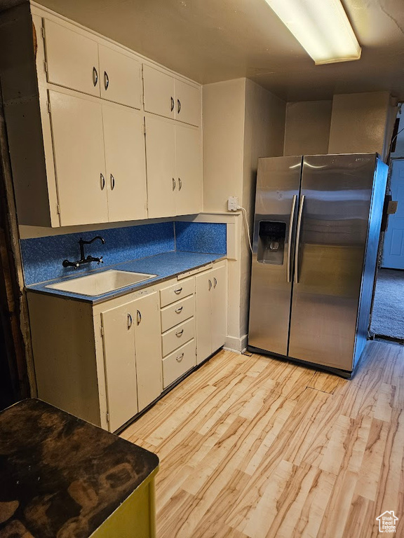 Kitchen with stainless steel fridge with ice dispenser, a sink, white cabinetry, and light wood-style flooring