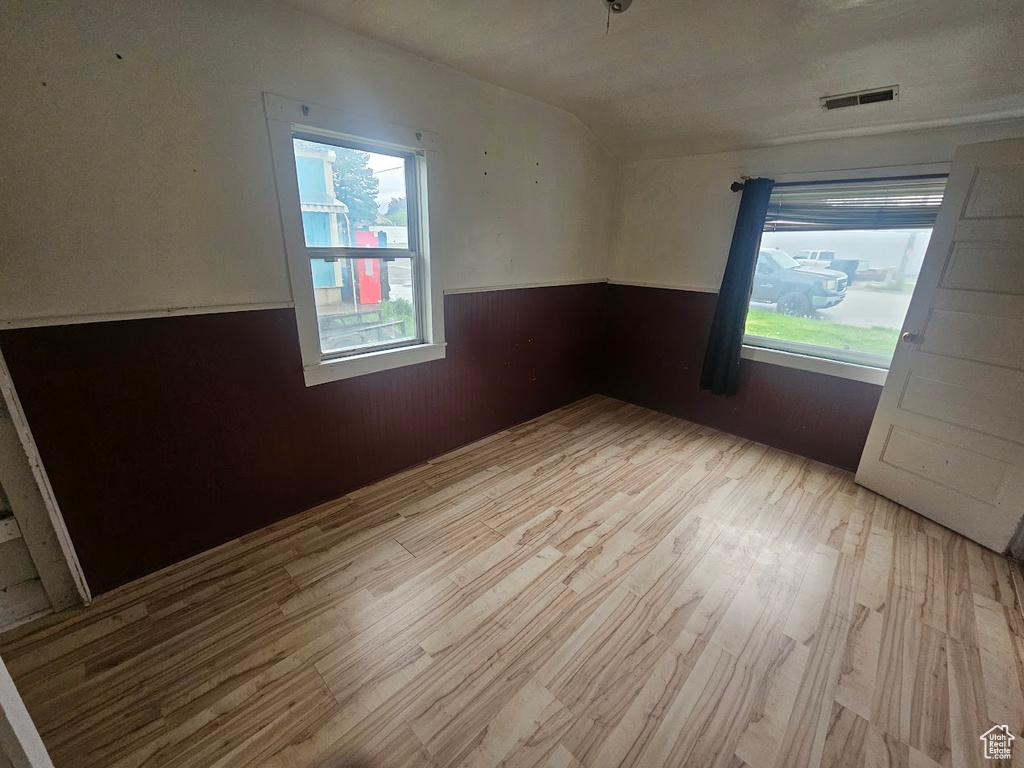Empty room with wainscoting, wood finished floors, vaulted ceiling, and wood walls