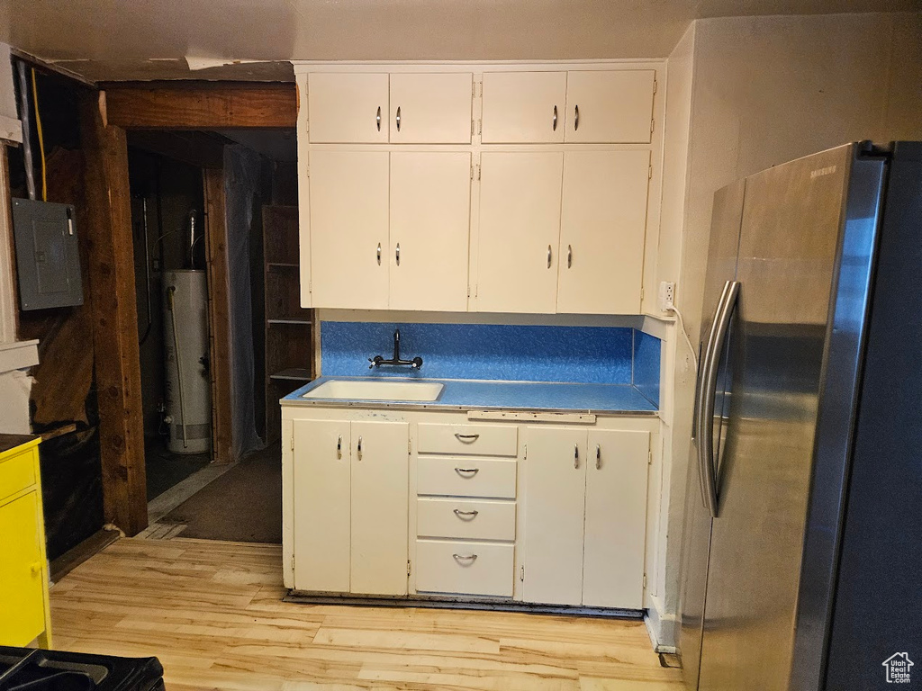 Kitchen featuring freestanding refrigerator, a sink, water heater, and white cabinets