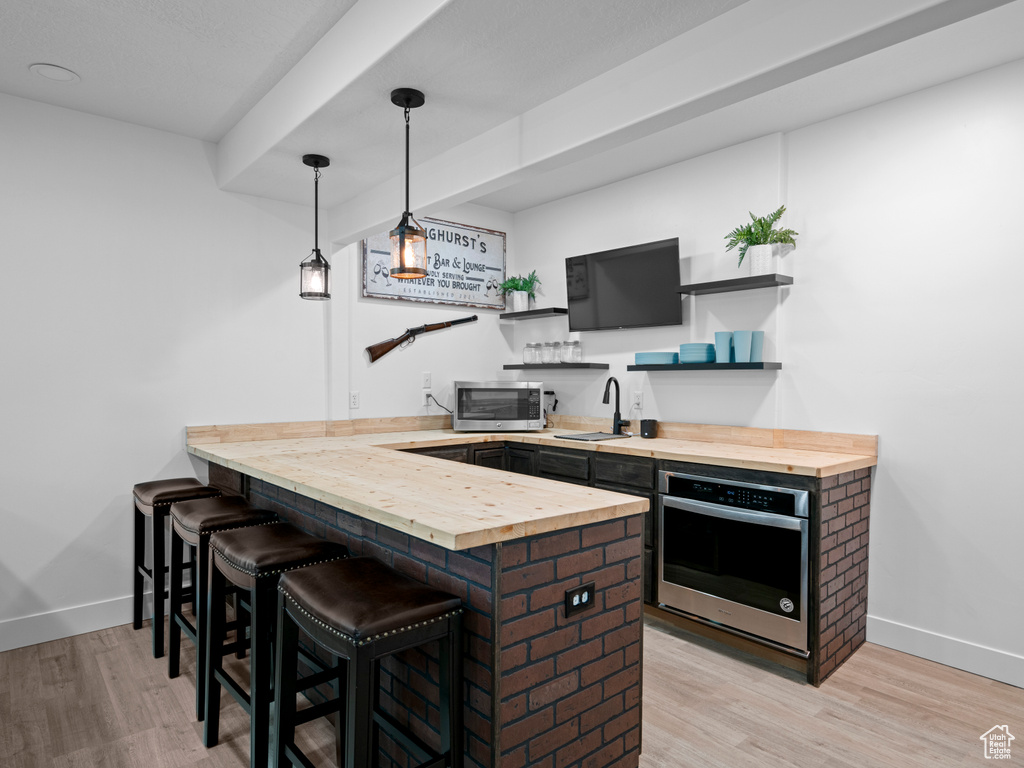 Indoor wet bar with stainless steel appliances, light wood-type flooring, baseboards, and pendant lighting