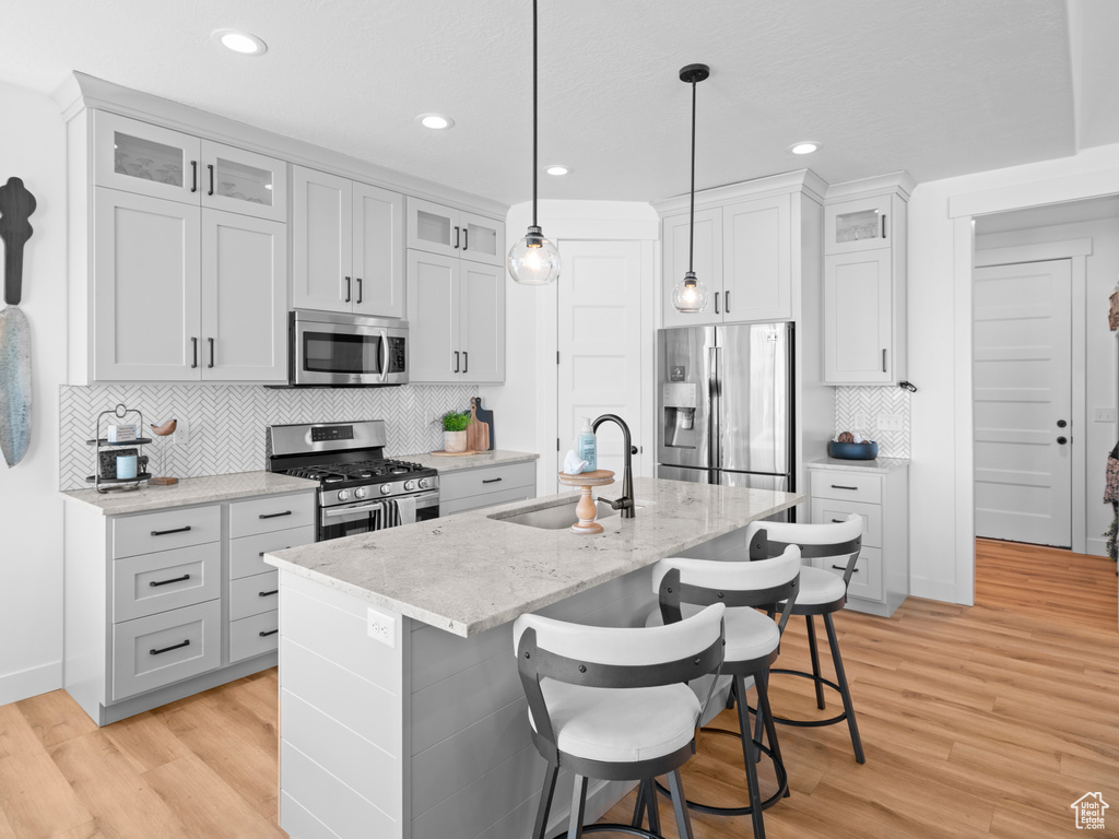 Kitchen with appliances with stainless steel finishes, a sink, light wood-style flooring, a center island with sink, and recessed lighting