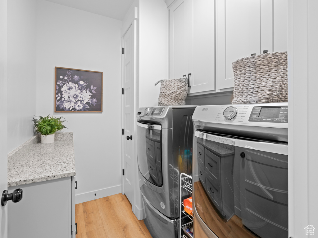Laundry area featuring cabinet space, washing machine and clothes dryer, light wood-style flooring, and baseboards