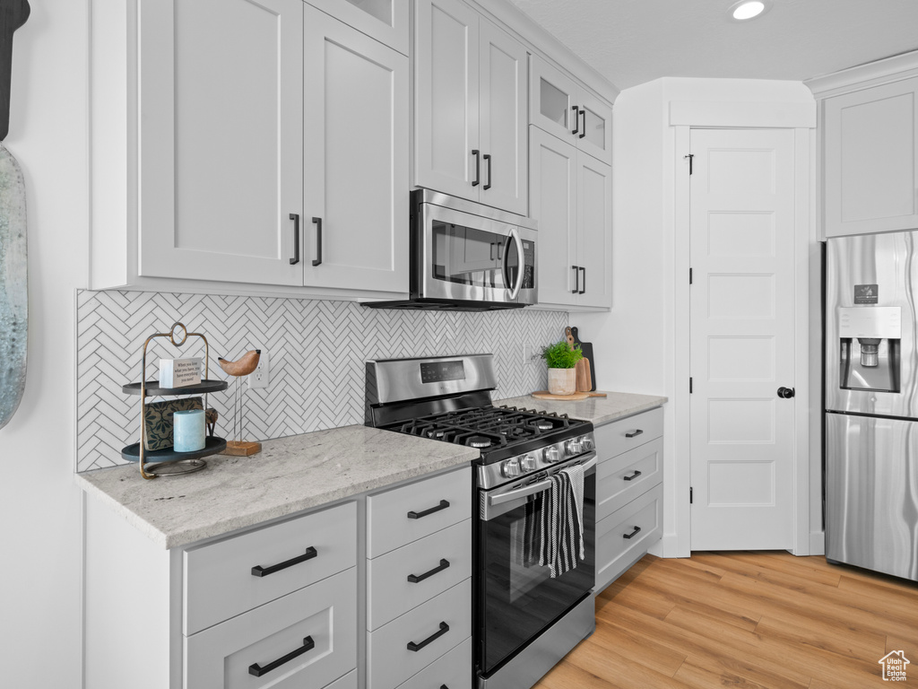 Kitchen featuring stainless steel appliances, light wood-style flooring, glass insert cabinets, backsplash, and light stone countertops