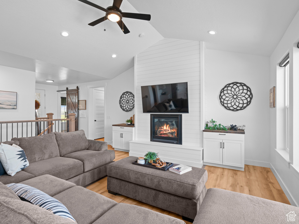 Living area with a barn door, a ceiling fan, light wood-style flooring, vaulted ceiling, and recessed lighting