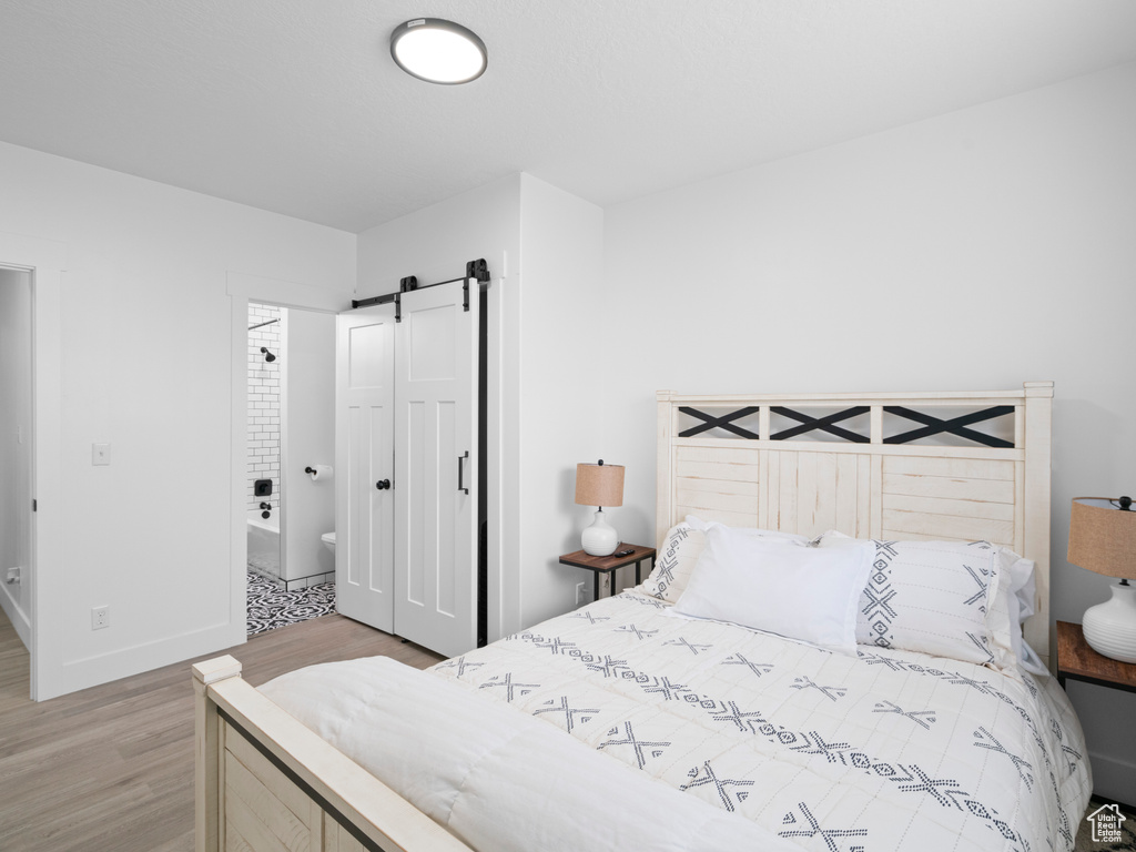Bedroom with light wood-type flooring, a barn door, and baseboards